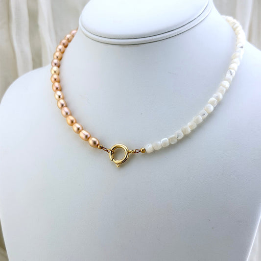 A delicate necklace displayed on a white jewelry bust, featuring champagne pink pearls on one side, mother-of-pearl beads on the other, and a gold clasp.